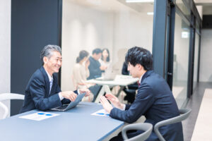 新入社員とOJT担当者が、落ち着いた雰囲気で資料を見ながら進捗や相談事項を確認している場面